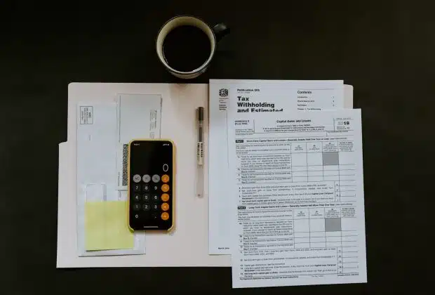 black Android smartphone near ballpoint pen, tax withholding certificate on top of white folder